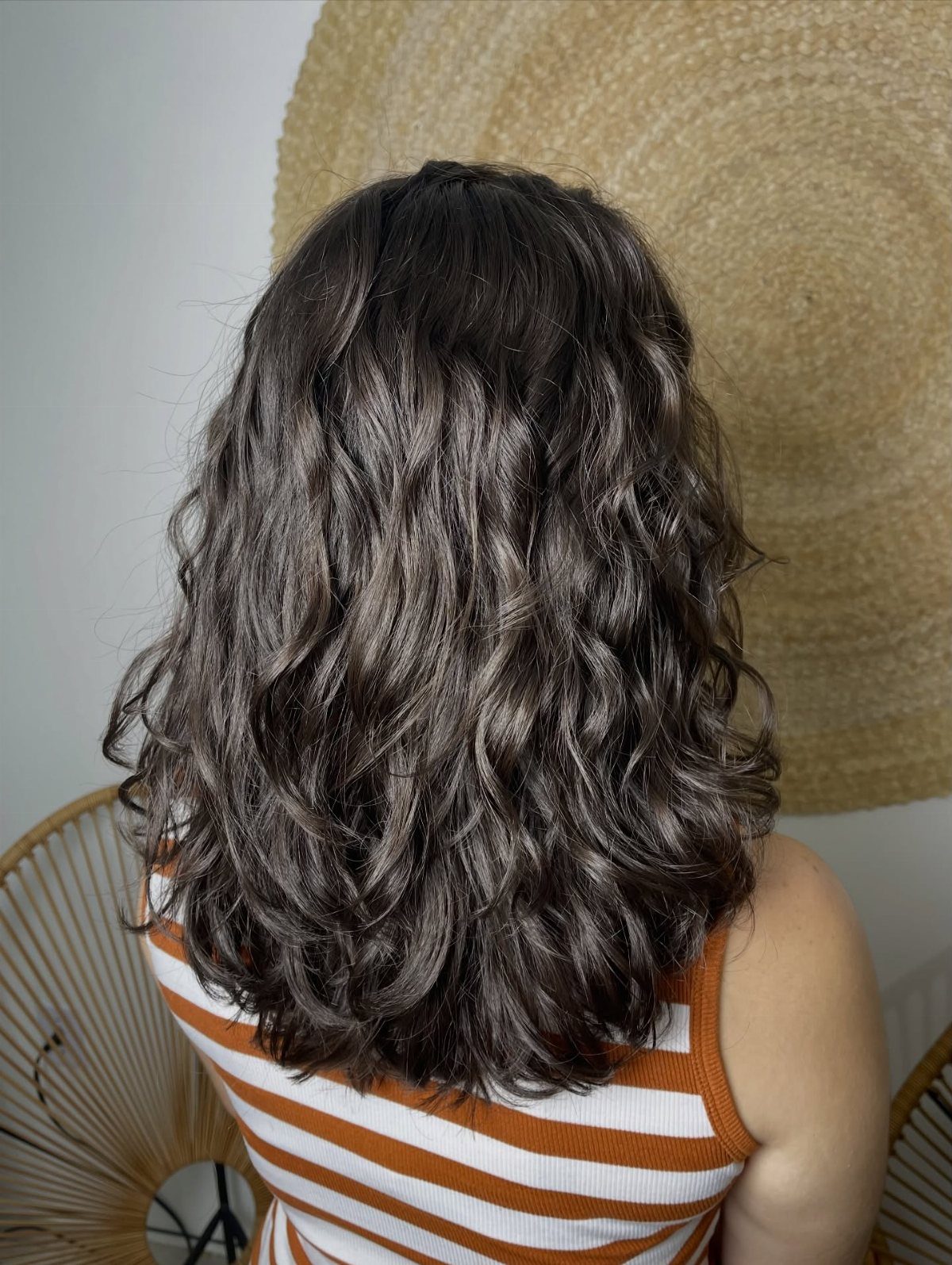 18 Medium Length Curly Hair Hairstyles, From Bobs to Shags 18 Medium length dark brown curly hair seen from behind against a white wall.