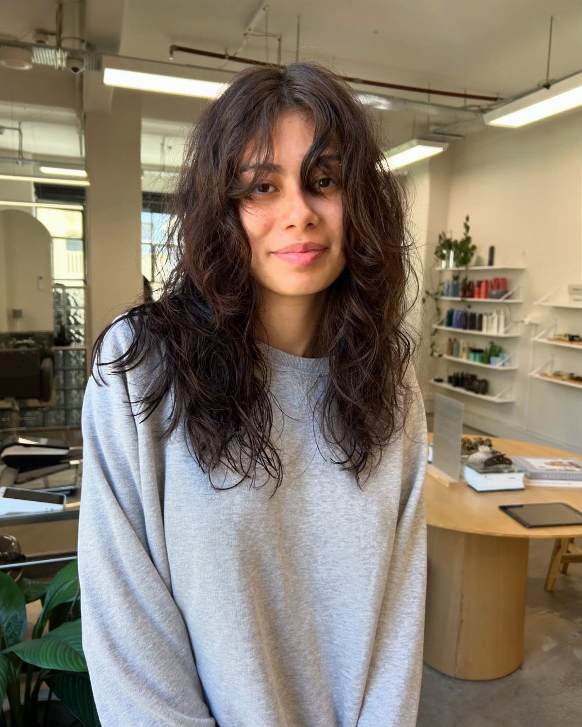 18 Medium Length Curly Hair Hairstyles, From Bobs to Shags 13 Woman with mid-length wavy dark brown hair and bangs in a hair salon