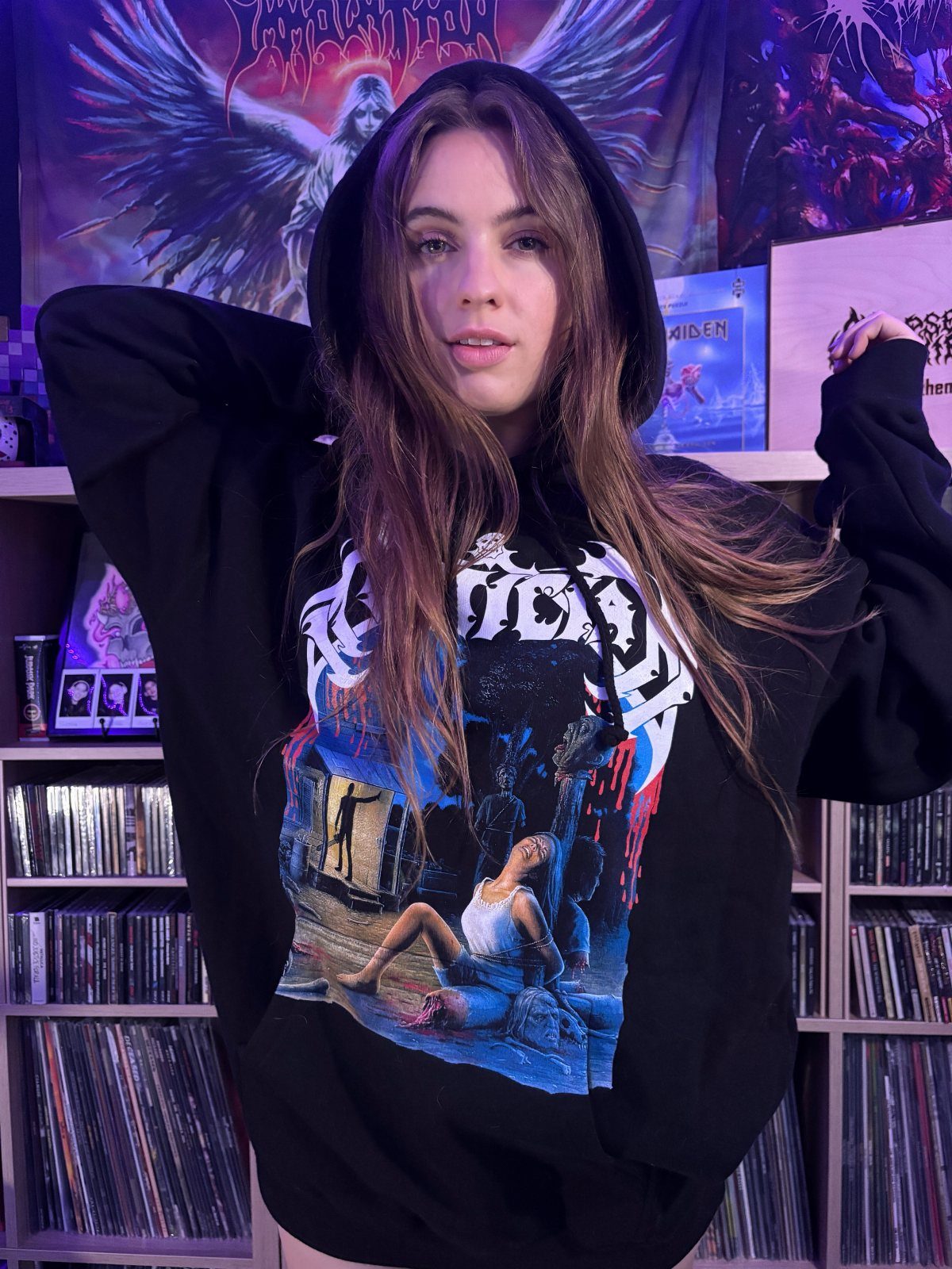 Metal Festival Outfit Ideas for Women: 10 Bold Looks to Try 5 Woman wearing a black metal band hoodie posing in front of CD shelves.