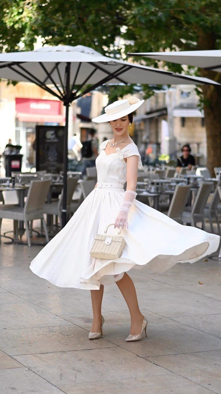 Woman in a vintage short white dress and hat posing outdoors at a cafe