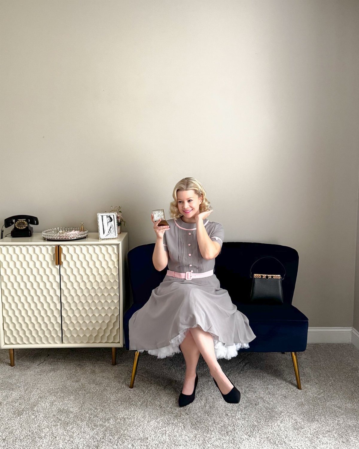 Woman in grey vintage dress and black pumps sitting on blue velvet sofa