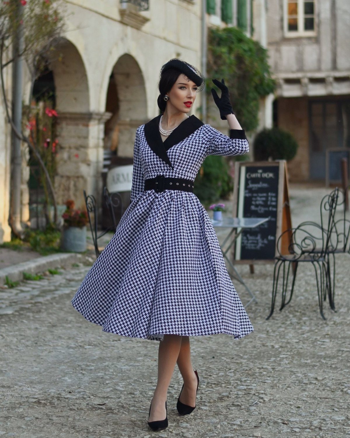 Woman in blue and white houndstooth dress with black accessories on cobblestone street