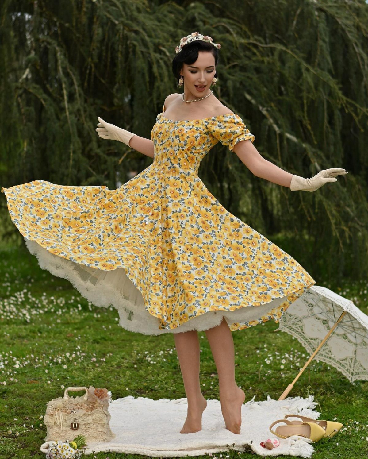 Woman in yellow floral vintage dress with full skirt and white gloves posing outdoors.