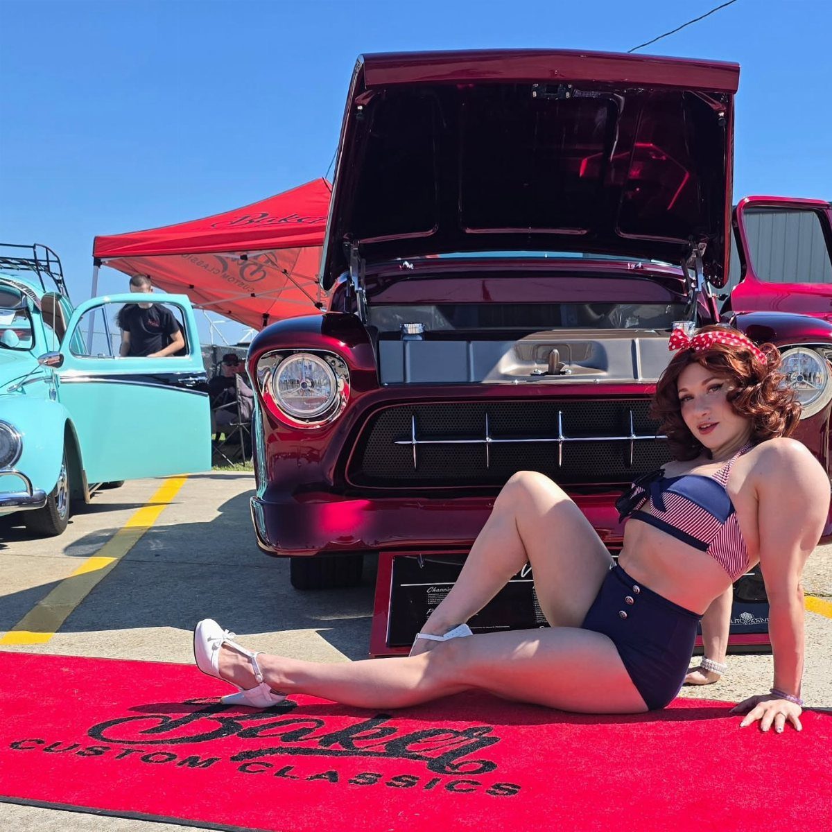 Pin Up Curls Hairstyles: 7 Ideas From Victory Rolls to Bows 8 Woman with vintage curls posing in front of a classic maroon car on red carpet.