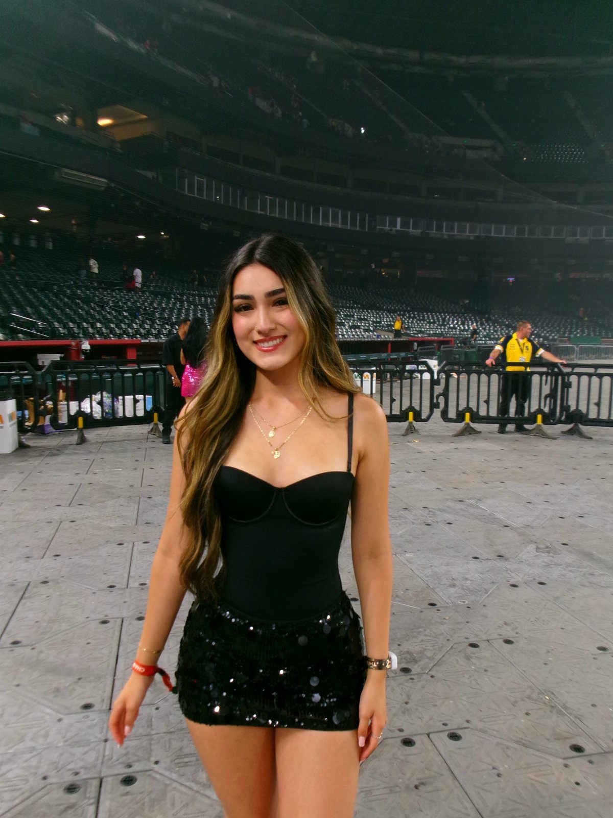 Woman in a black bodysuit and black sequined mini skirt at a stadium.