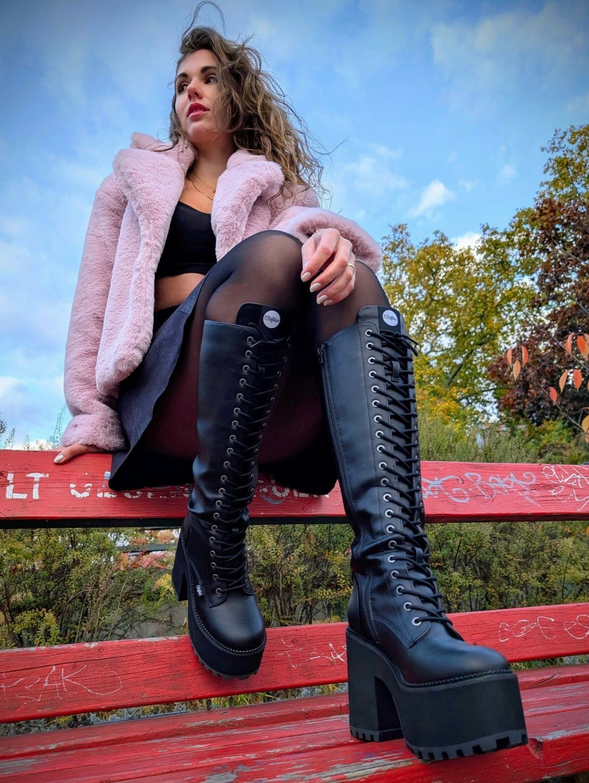 Woman wearing tall black platform combat boots sitting on a red wooden bench.