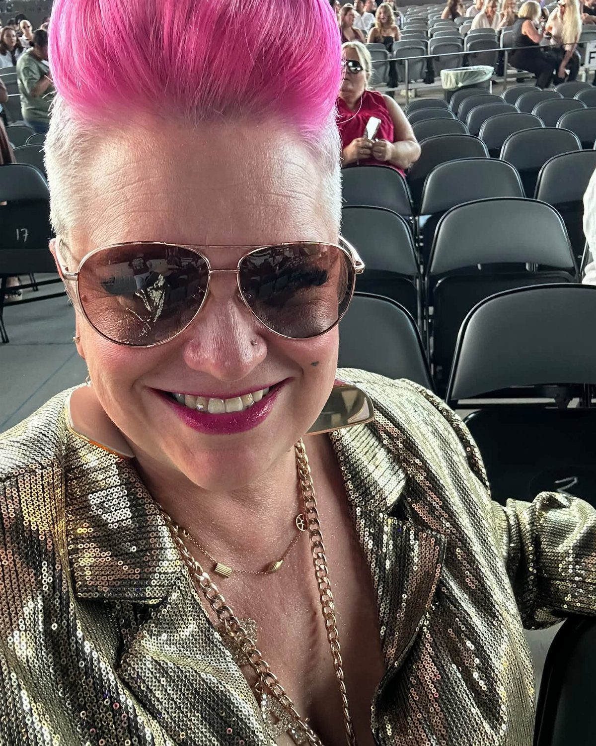Woman with pink hair wearing a gold metallic sequined jacket and gold necklaces.