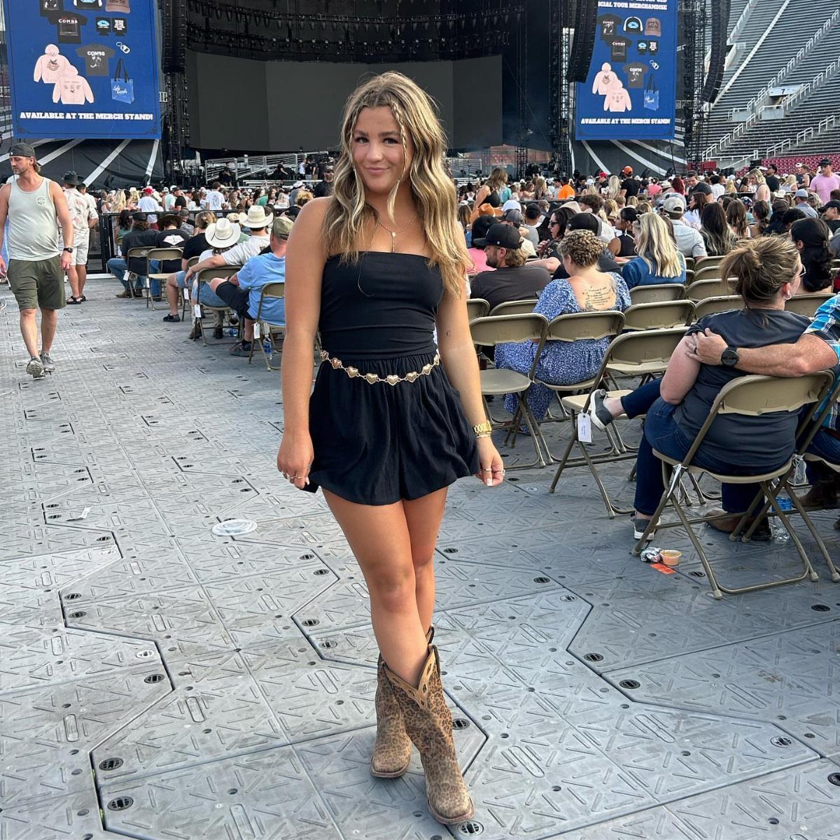 Woman in black mini dress and cowboy boots posing at outdoor concert venue