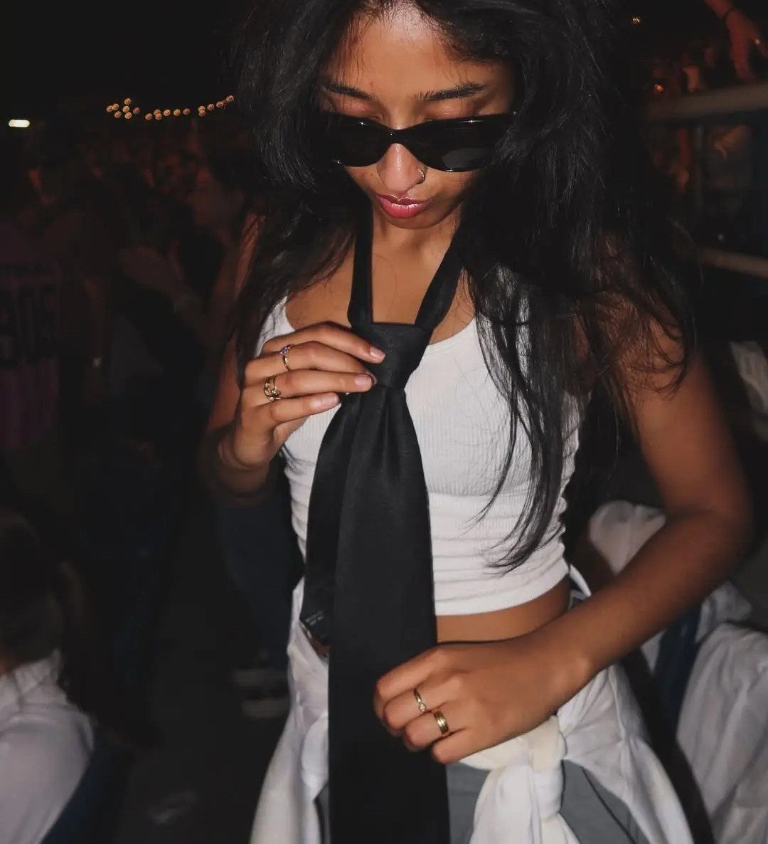 Woman wearing a white crop top and black tie at a night event.