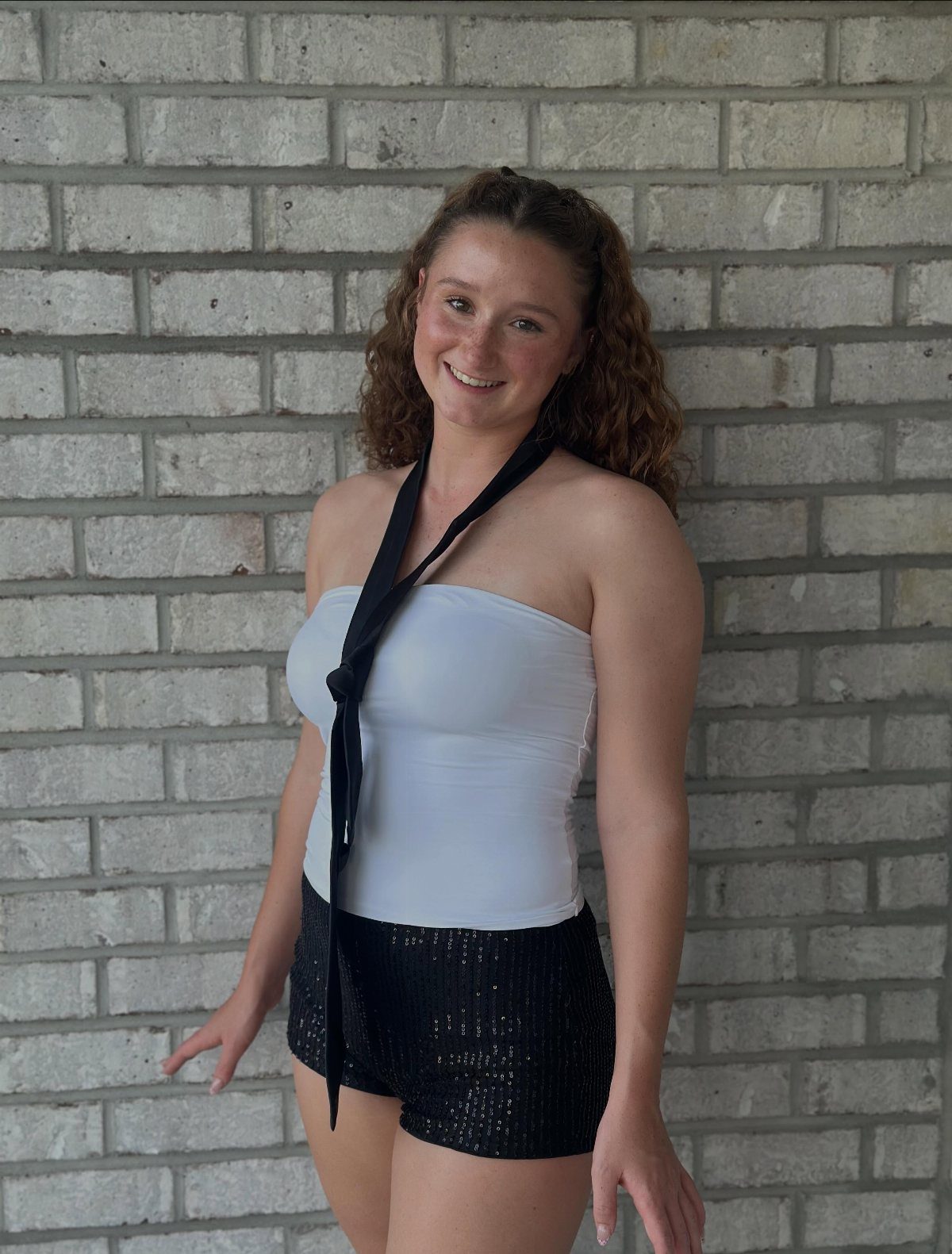 Woman wearing a white tube top and black sequined shorts against a brick wall.