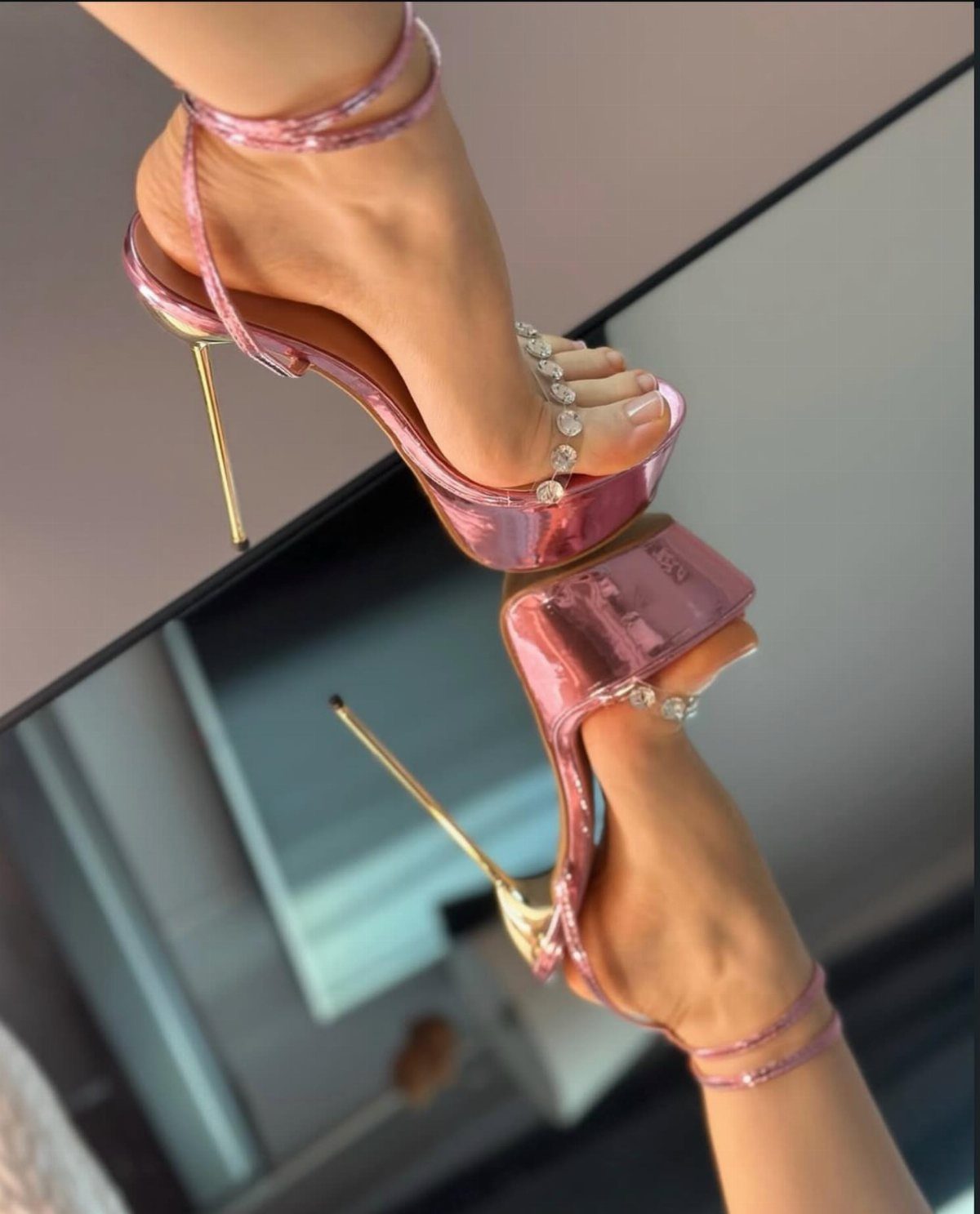 Metallic pink high-heeled sandals with gold stilettos reflected in a mirror.