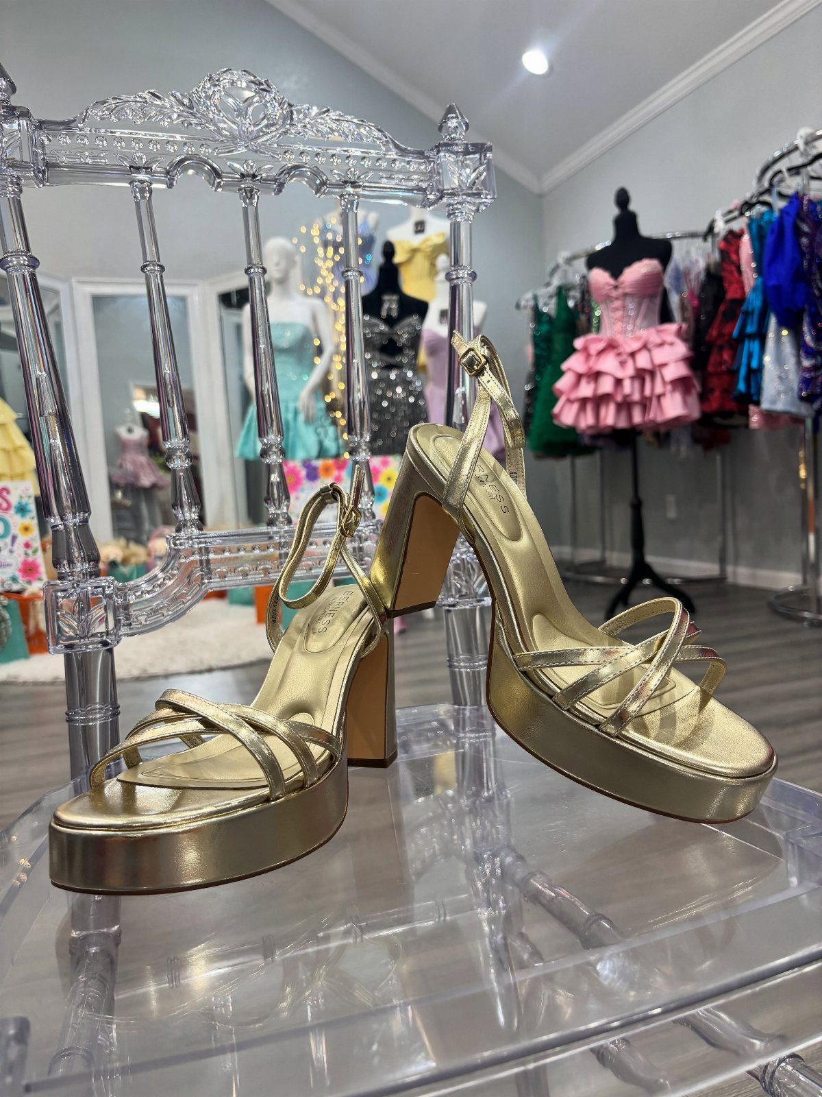 Gold platform heeled sandals resting on a clear acrylic chair in a dress shop.