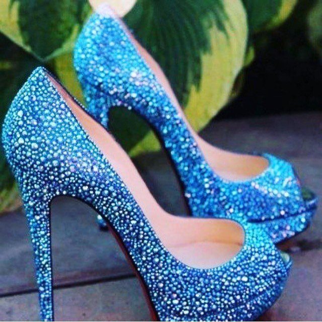 Blue high-heeled pumps covered in sparkling rhinestones against a green leafy background.