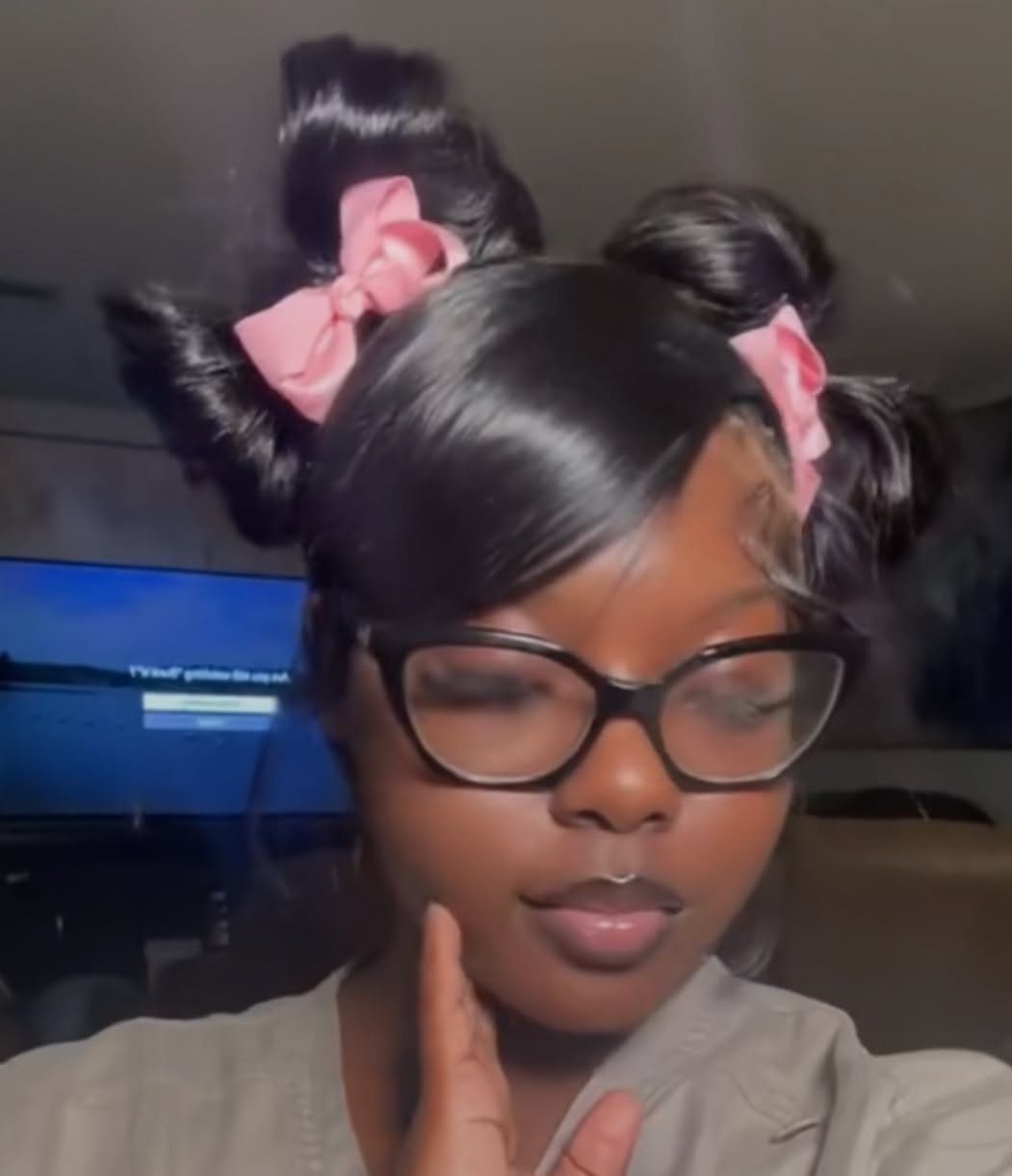 Person with two high hair puffs decorated with pink bows and black glasses