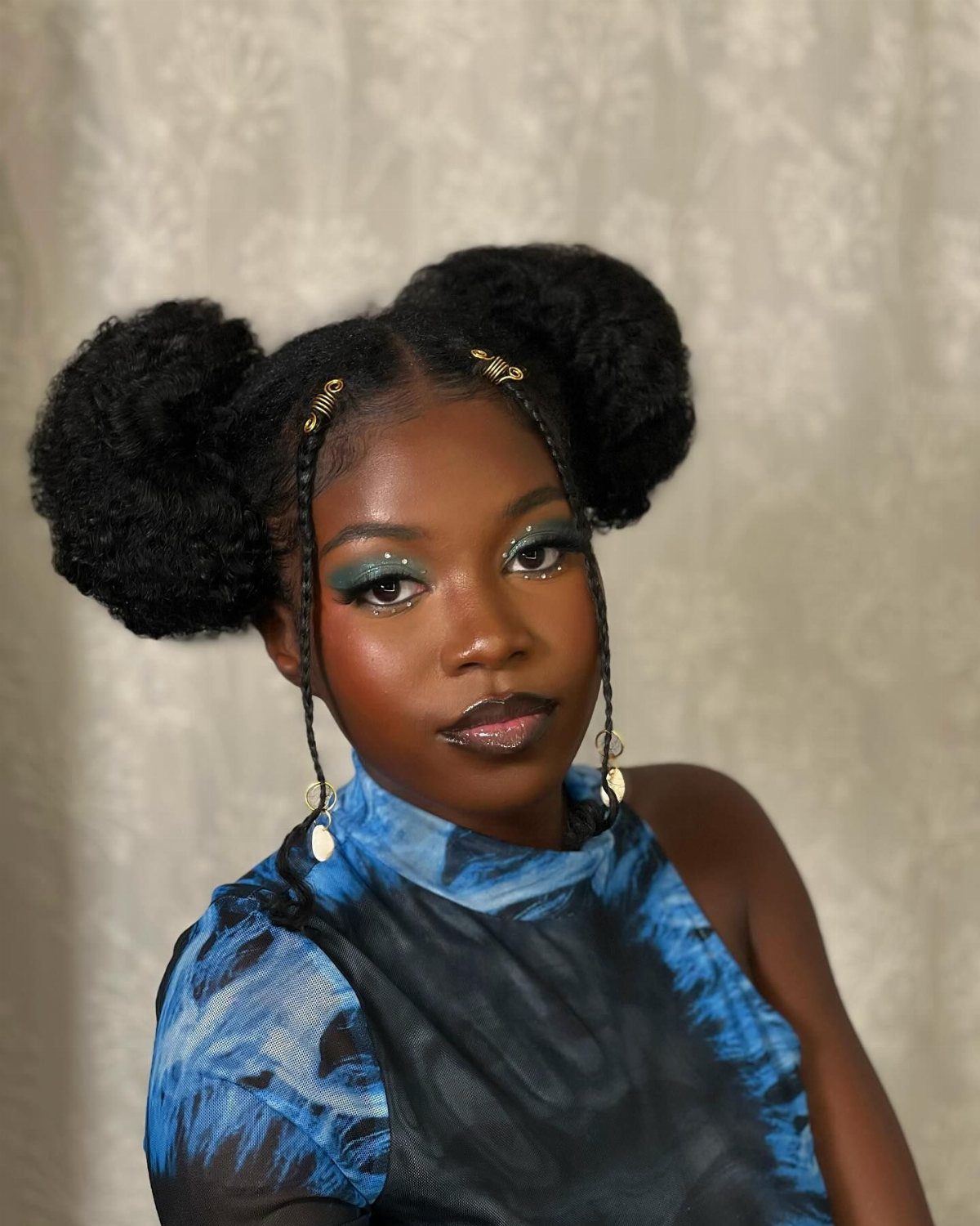 Person with two high afro puffs and thin braids framing the face with gold cuffs.
