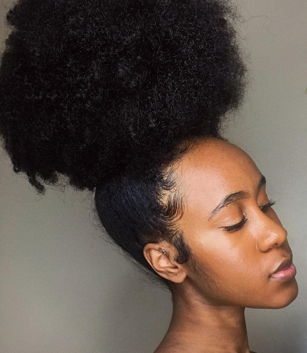 Woman with dark skin featuring a large, voluminous single high puff hairstyle.
