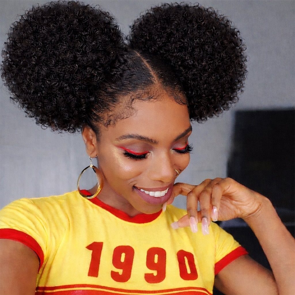 Woman with two high afro puffs, wearing a yellow 1990 t-shirt and gold hoops.