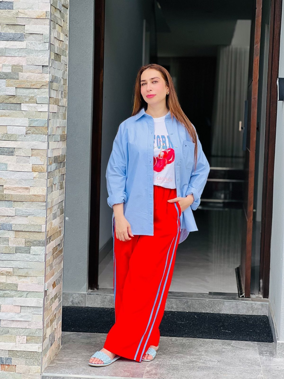 Woman wearing an oversized light blue button-down shirt and red wide-leg track pants.