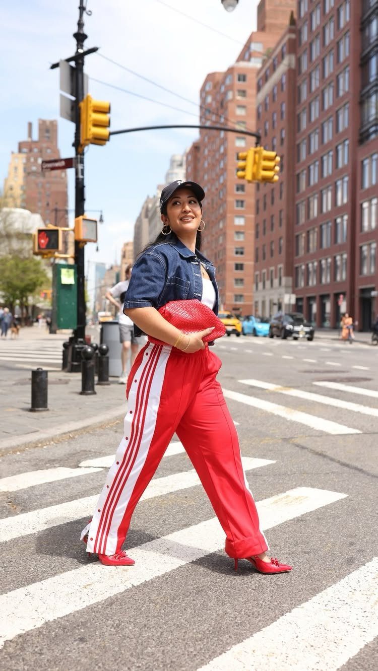 Woman in red track pants and denim jacket walking across a city street.