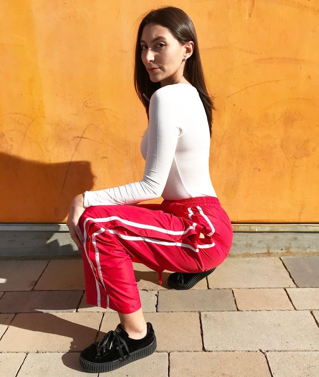 Woman wearing a white long-sleeve top and red track pants with black sneakers.