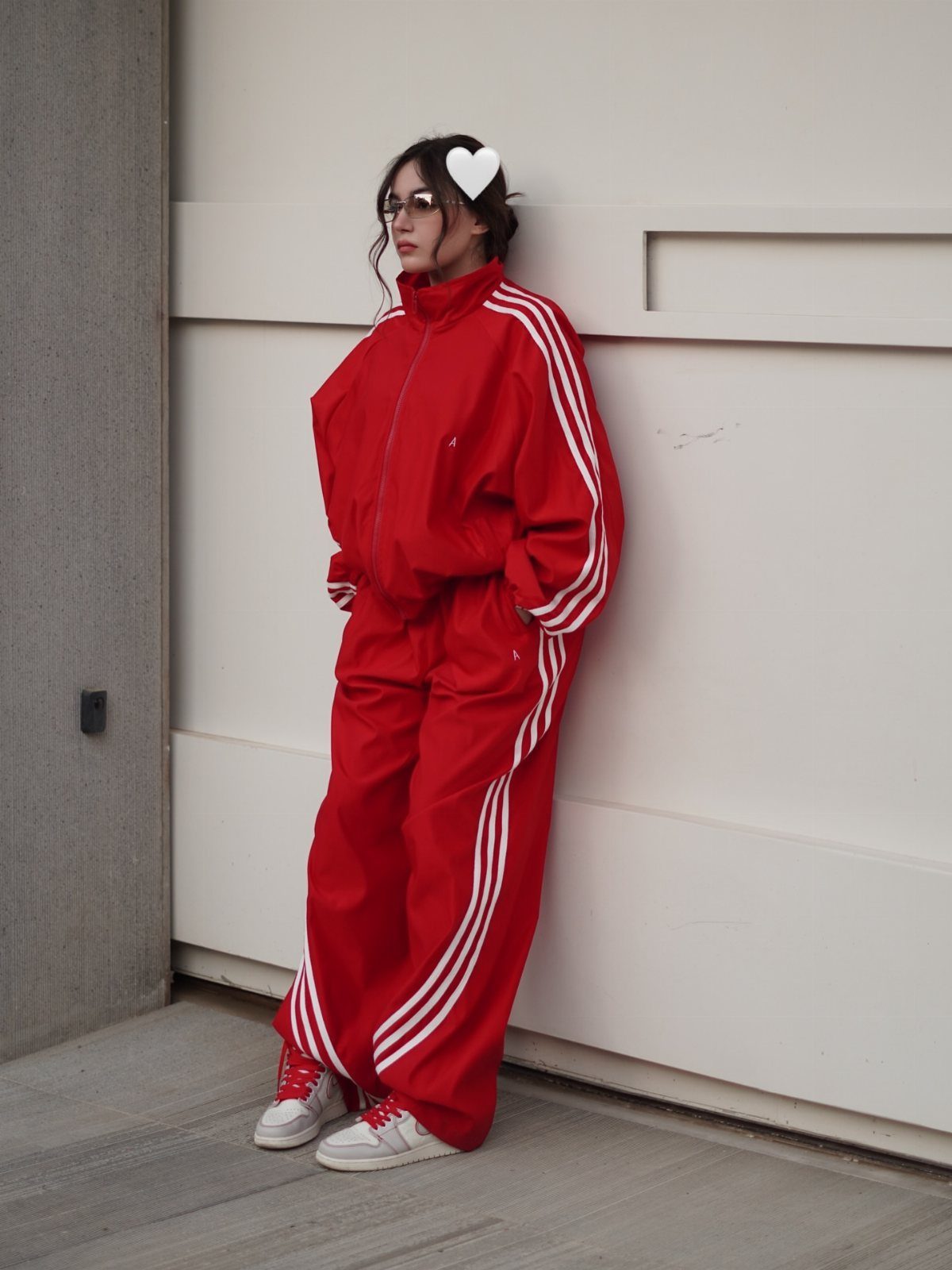Woman in a red Adidas tracksuit and sneakers posing against a white wall
