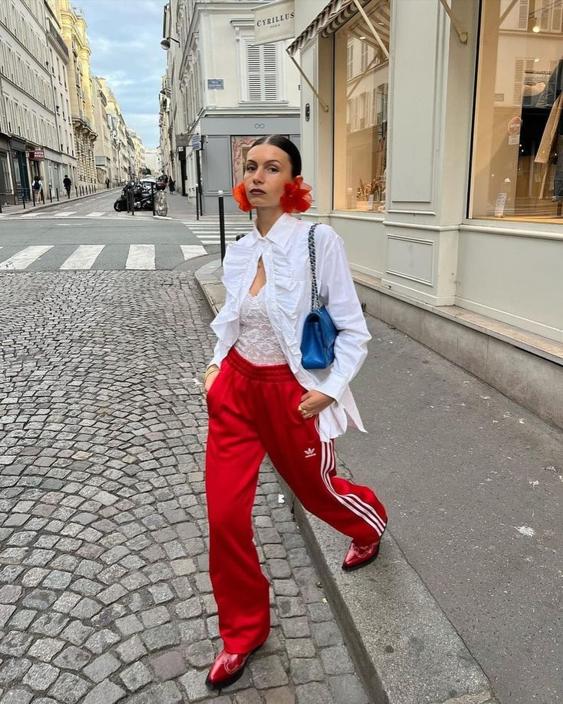 Woman wearing a white button-down shirt and red Adidas track pants on a street.