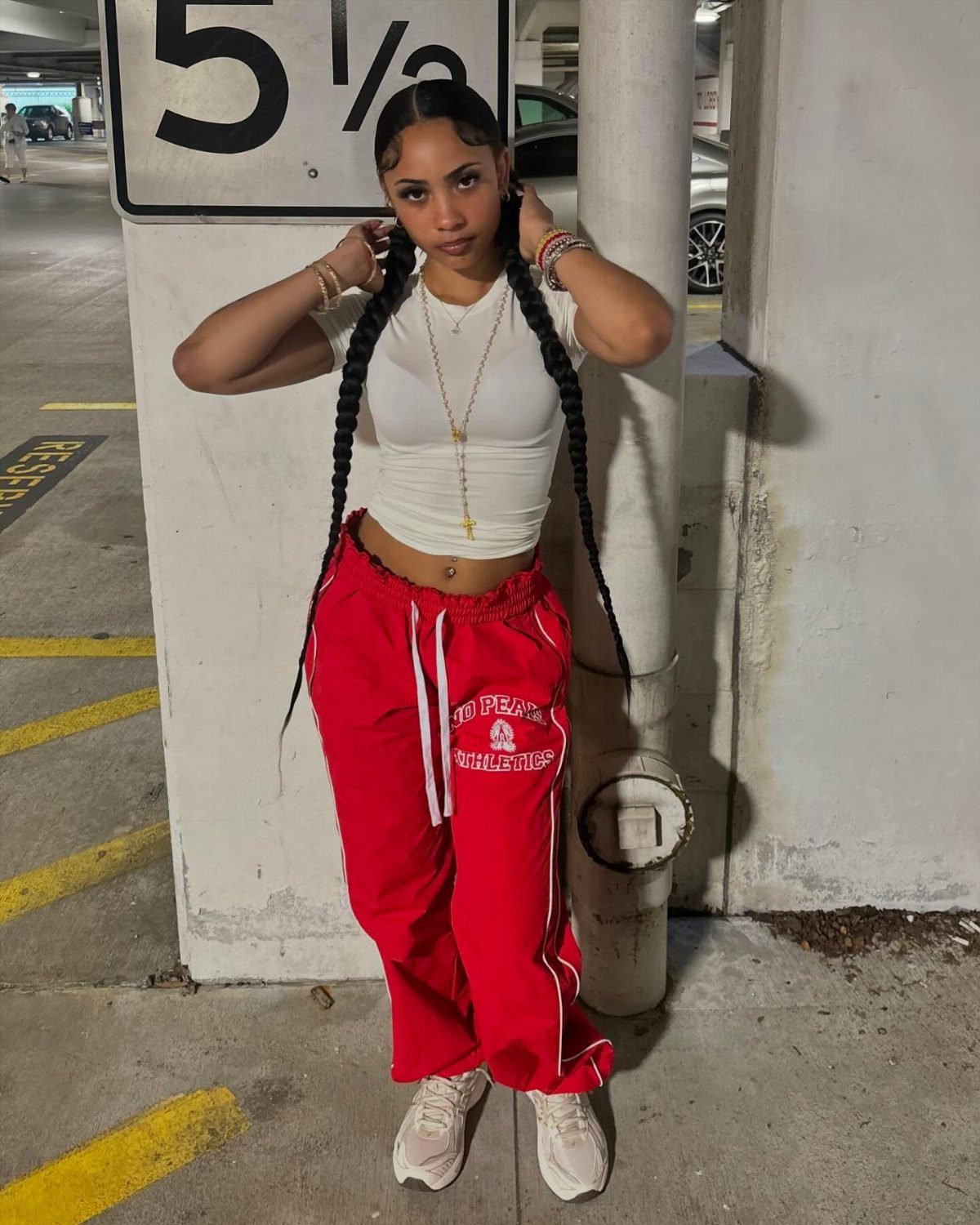 Woman in white cropped tee and red track pants posing in a parking garage.