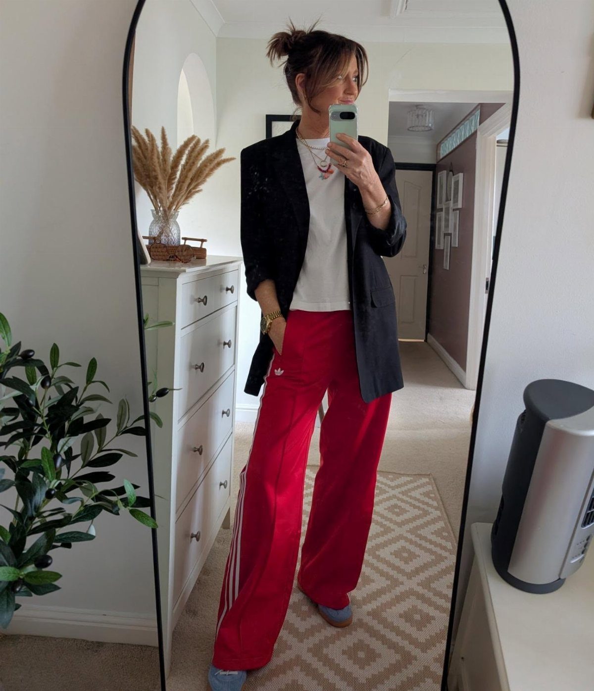 Woman wearing a black blazer, white tee, and red Adidas track pants.