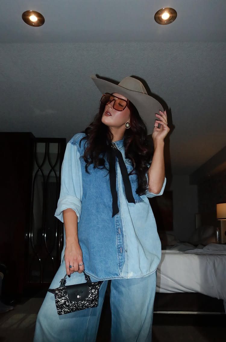 29 Rodeo Inspired Outfits Built on Fringe, Denim, and Boots 11 Woman in a denim-on-denim outfit with a grey cowboy hat and red sunglasses.