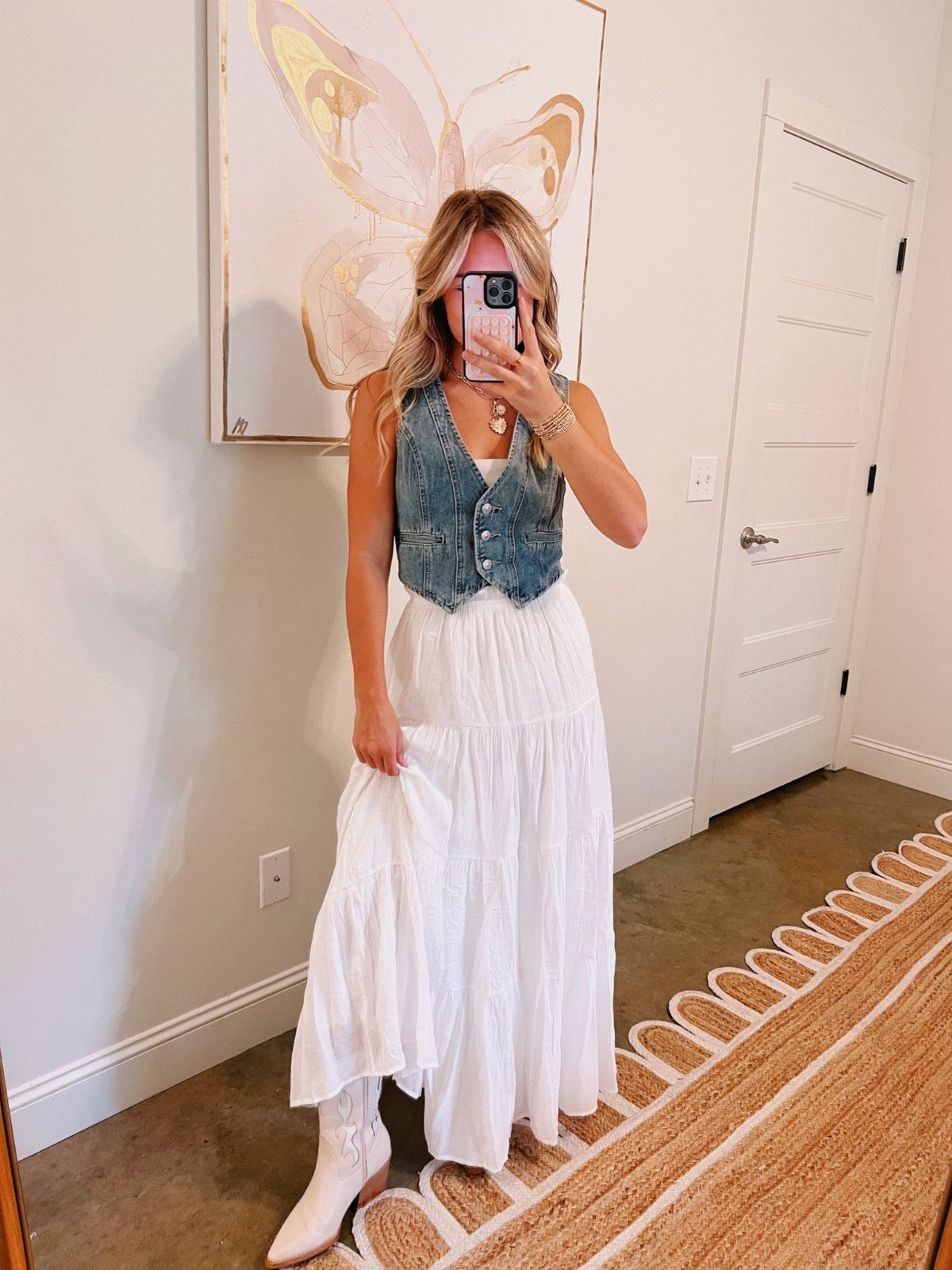29 Rodeo Inspired Outfits Built on Fringe, Denim, and Boots 23 Woman wearing a cropped denim vest and a tiered white maxi skirt with boots.