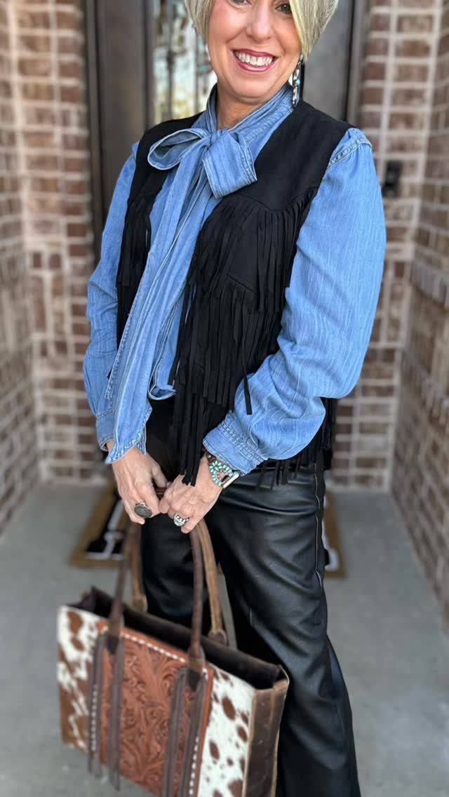 29 Rodeo Inspired Outfits Built on Fringe, Denim, and Boots 6 Woman wearing a black fringe vest over a blue shirt and leather pants.