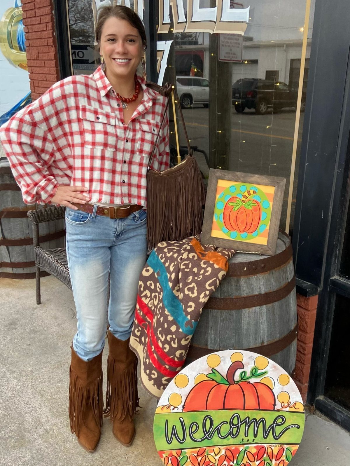 29 Rodeo Inspired Outfits Built on Fringe, Denim, and Boots 7 Woman in red plaid shirt and fringe boots standing by autumn decorations.