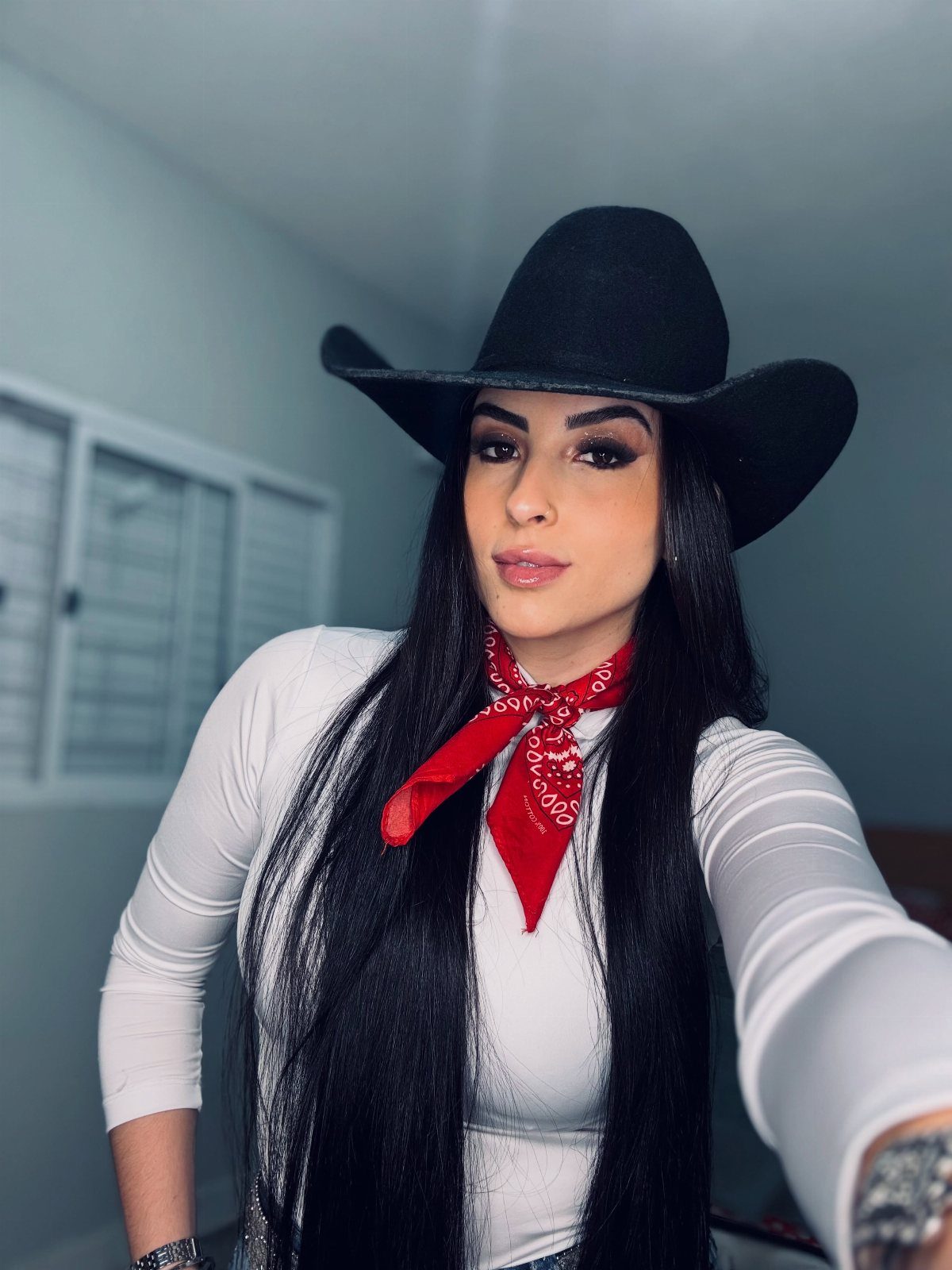 29 Rodeo Inspired Outfits Built on Fringe, Denim, and Boots 20 Woman wearing a black cowboy hat, white top, and red paisley bandana.