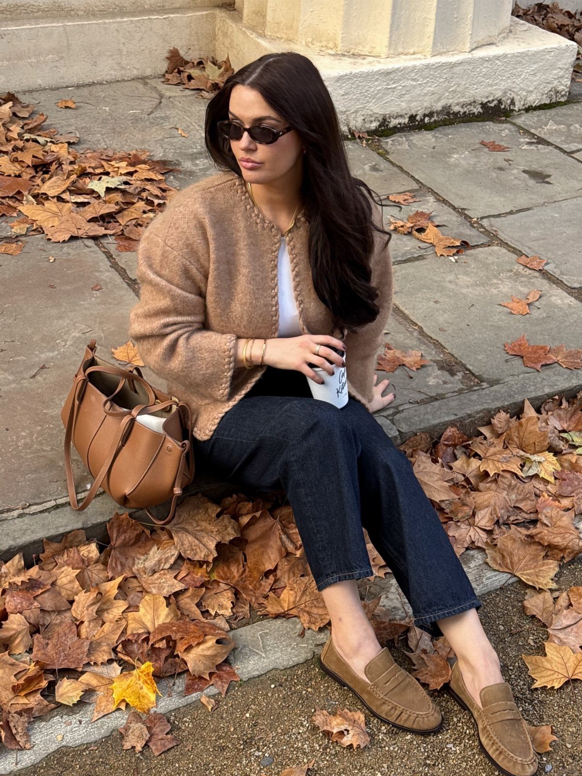 Semi Casual Clothes: 31 Outfit Ideas From Dresses to Loafers 9 Woman in brown knit cardigan and dark jeans sitting among autumn leaves.