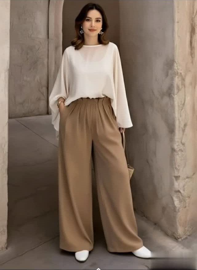 Semi Casual Clothes: 31 Outfit Ideas From Dresses to Loafers 15 Woman wearing a white blouse and wide-leg tan trousers in a stone hallway.