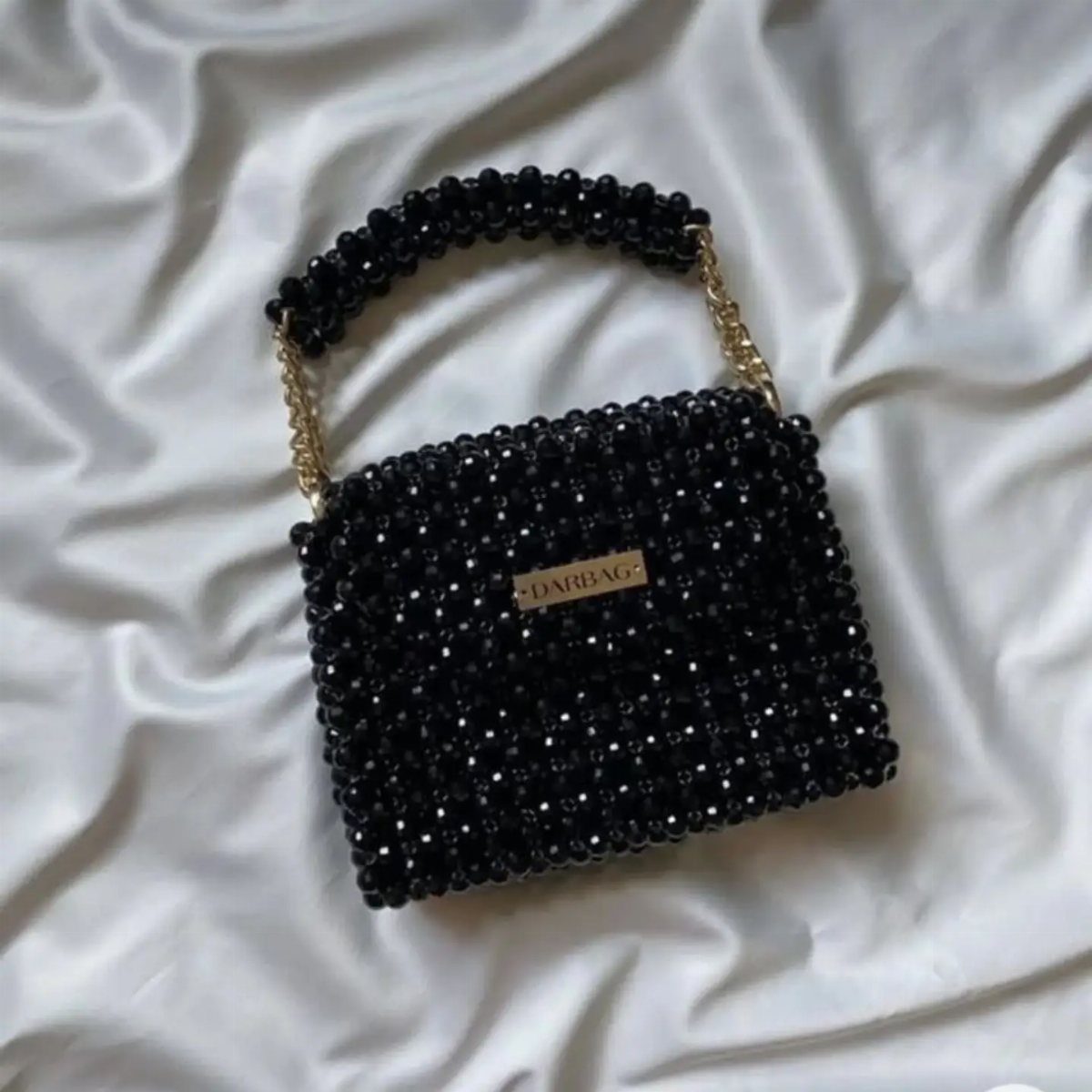 12 Seventeen Concert Outfit Ideas for Women to Stand Out 5 Black beaded handbag with gold chain on white satin fabric.