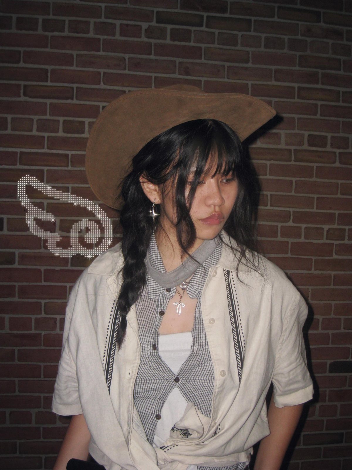 12 Seventeen Concert Outfit Ideas for Women to Stand Out 6 Woman wearing a brown cowboy hat and white shirt against a brick wall.