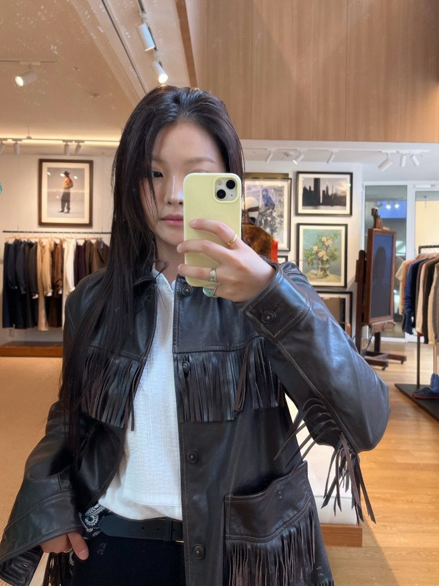 12 Seventeen Concert Outfit Ideas for Women to Stand Out 7 Woman wearing a dark brown leather jacket with fringe detailing in a clothing store.