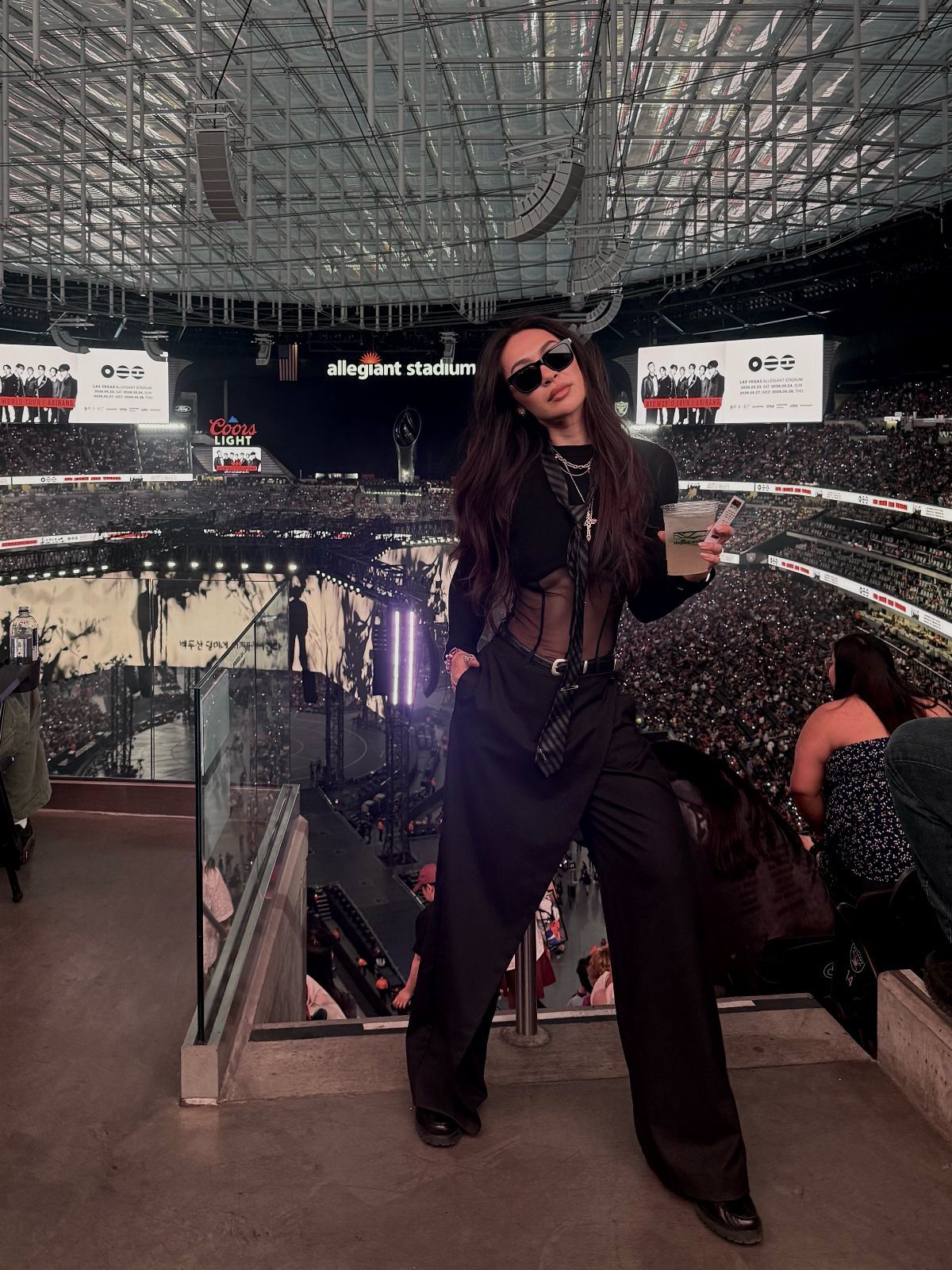 12 Seventeen Concert Outfit Ideas for Women to Stand Out 10 Woman in sheer black top, bra, and wide-leg trousers at a stadium concert.