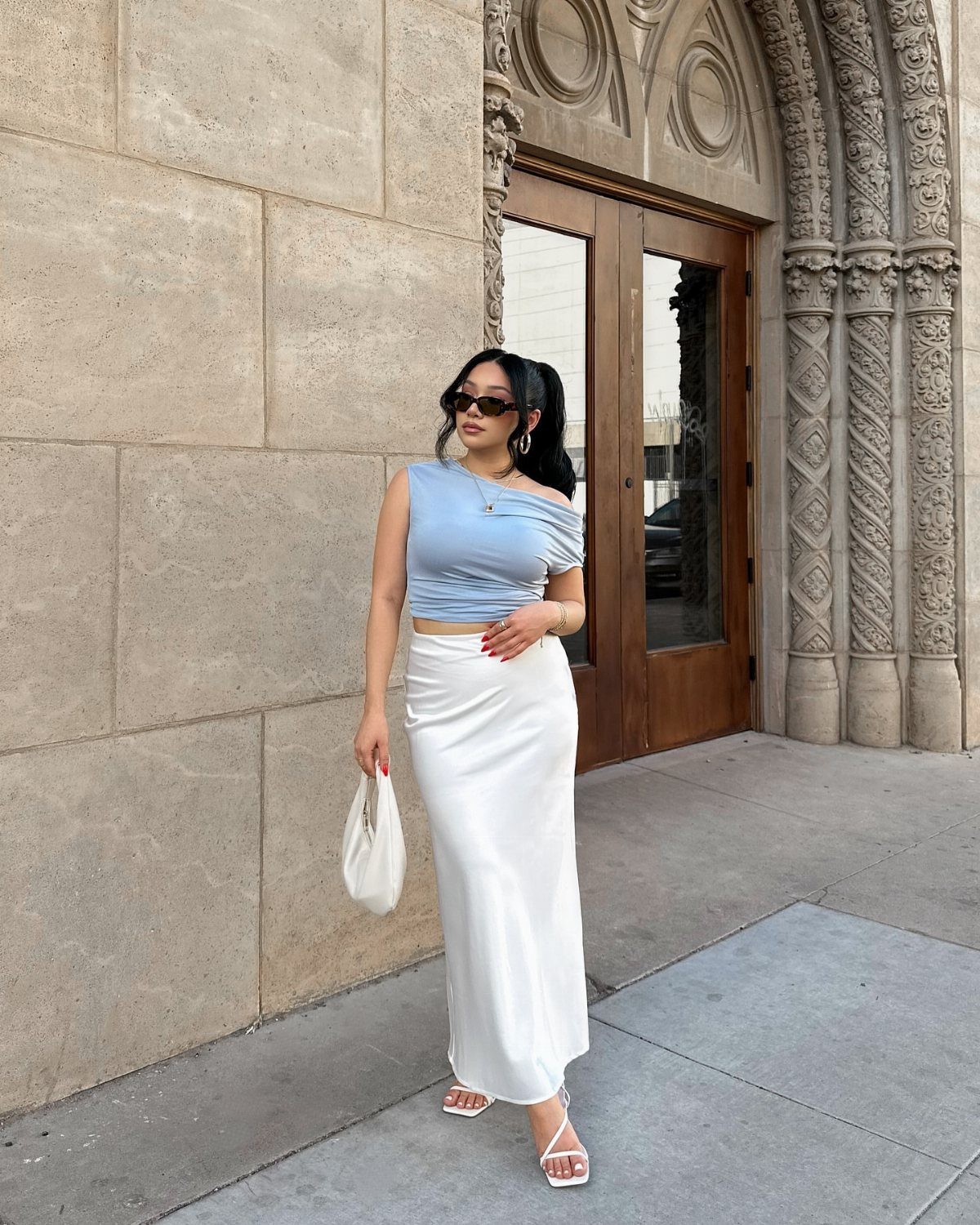 12 Seventeen Concert Outfit Ideas for Women to Stand Out 9 Woman wearing a blue one-shoulder tank top and white satin midi skirt outdoors.
