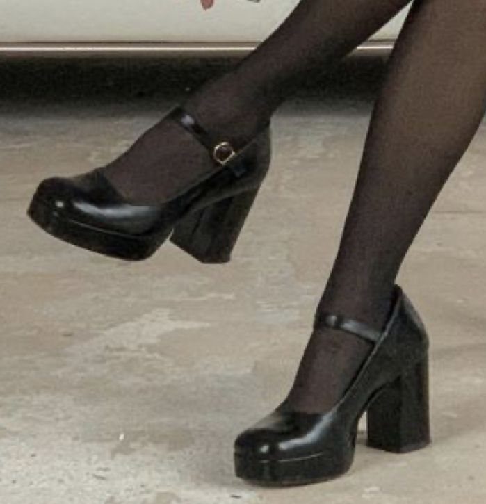 Black platform high heels worn with black sheer tights on a concrete floor.