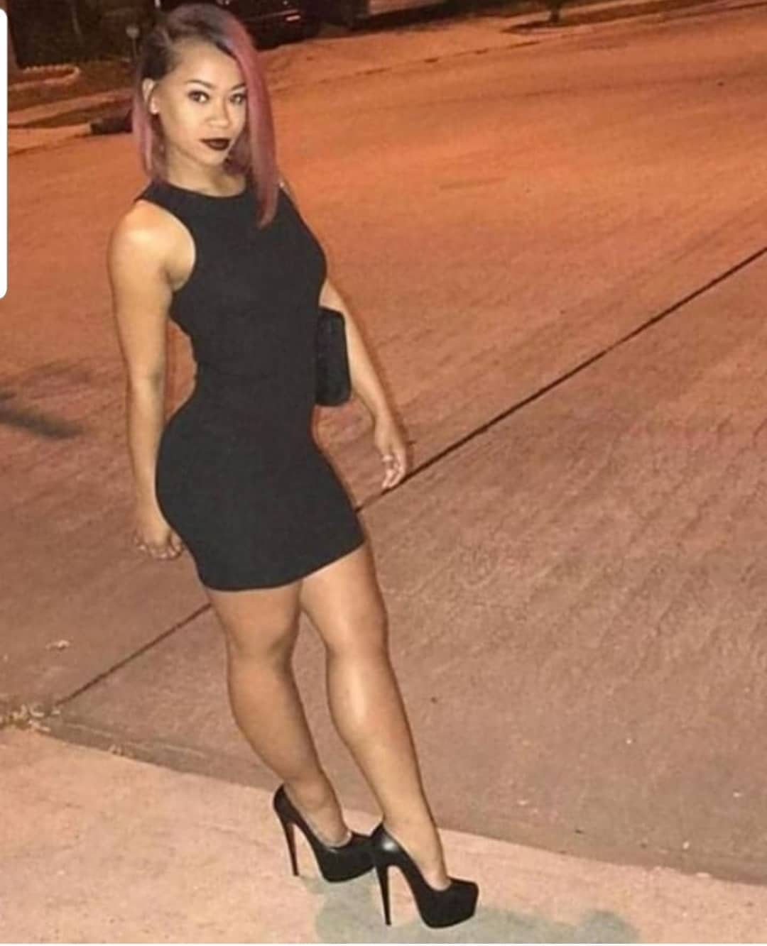 Woman in a short black dress wearing black platform high heels on a street.