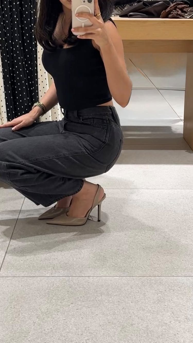 Person wearing dark grey jeans and beige stiletto heels in a mirror selfie.
