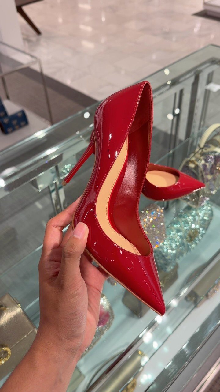 Red patent leather pump with pointed toe and stiletto heel held by hand