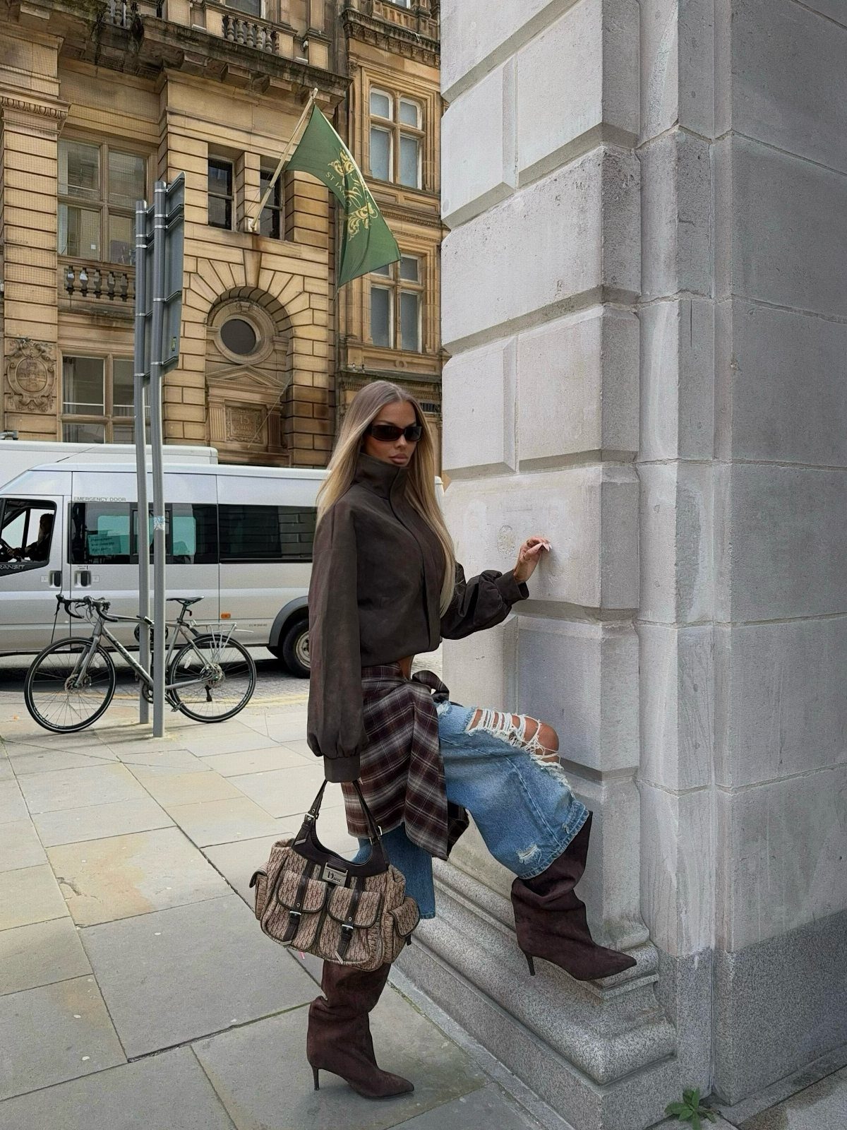 Woman wearing brown suede heeled boots and blue jeans leaning against a stone wall.