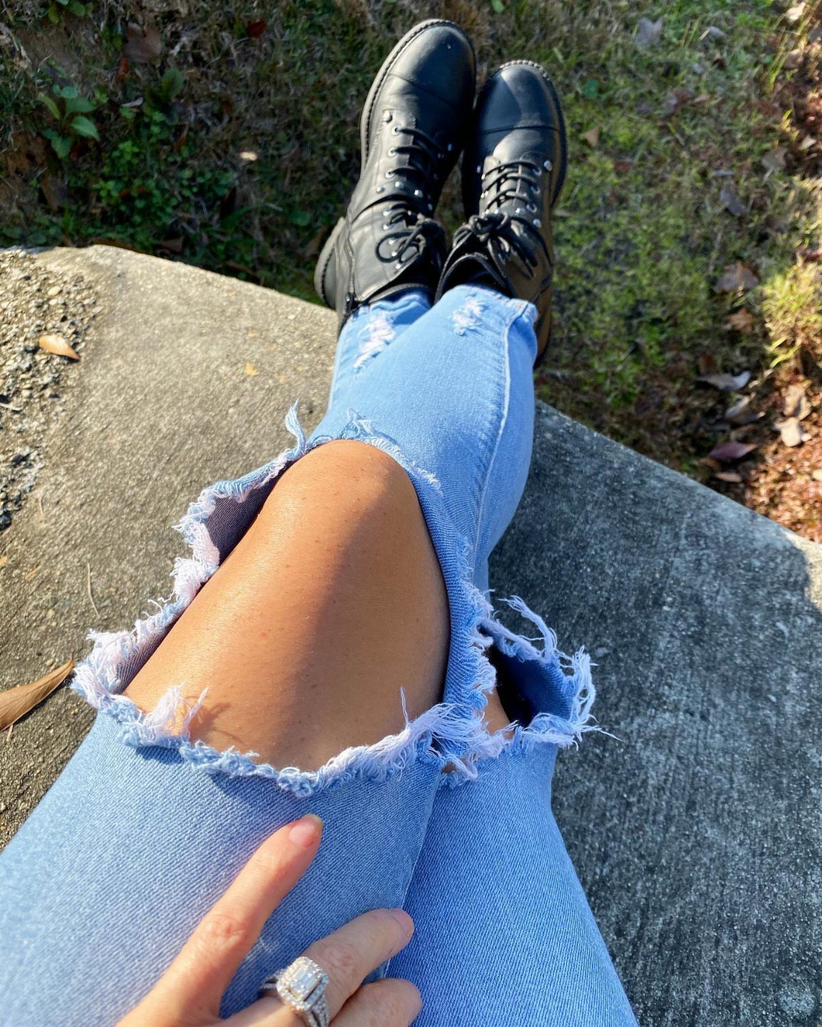Light-wash distressed jeans paired with black lace-up combat boots on a concrete ledge.