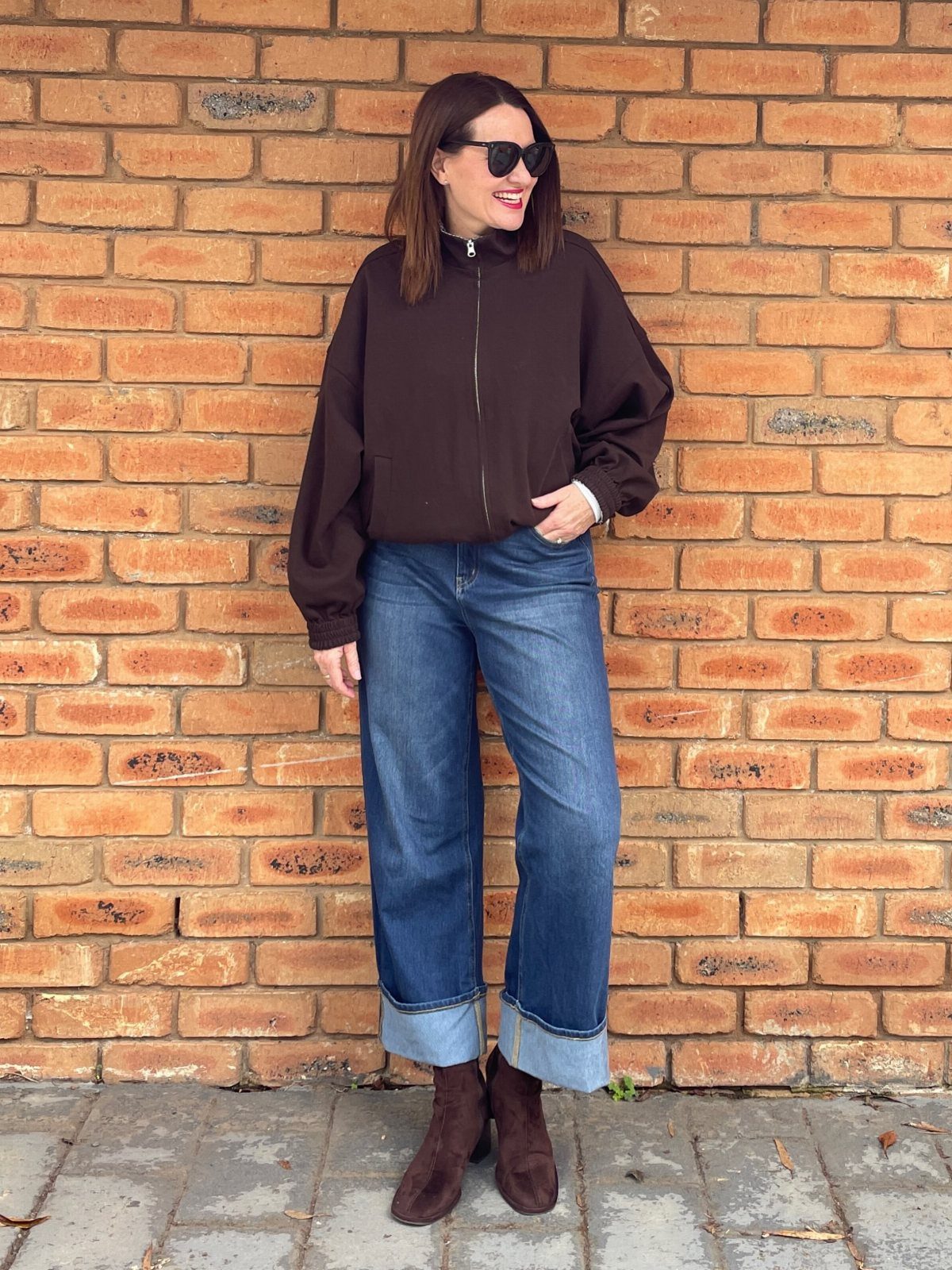 Woman wearing cuffed straight blue jeans and brown suede ankle boots against brick wall