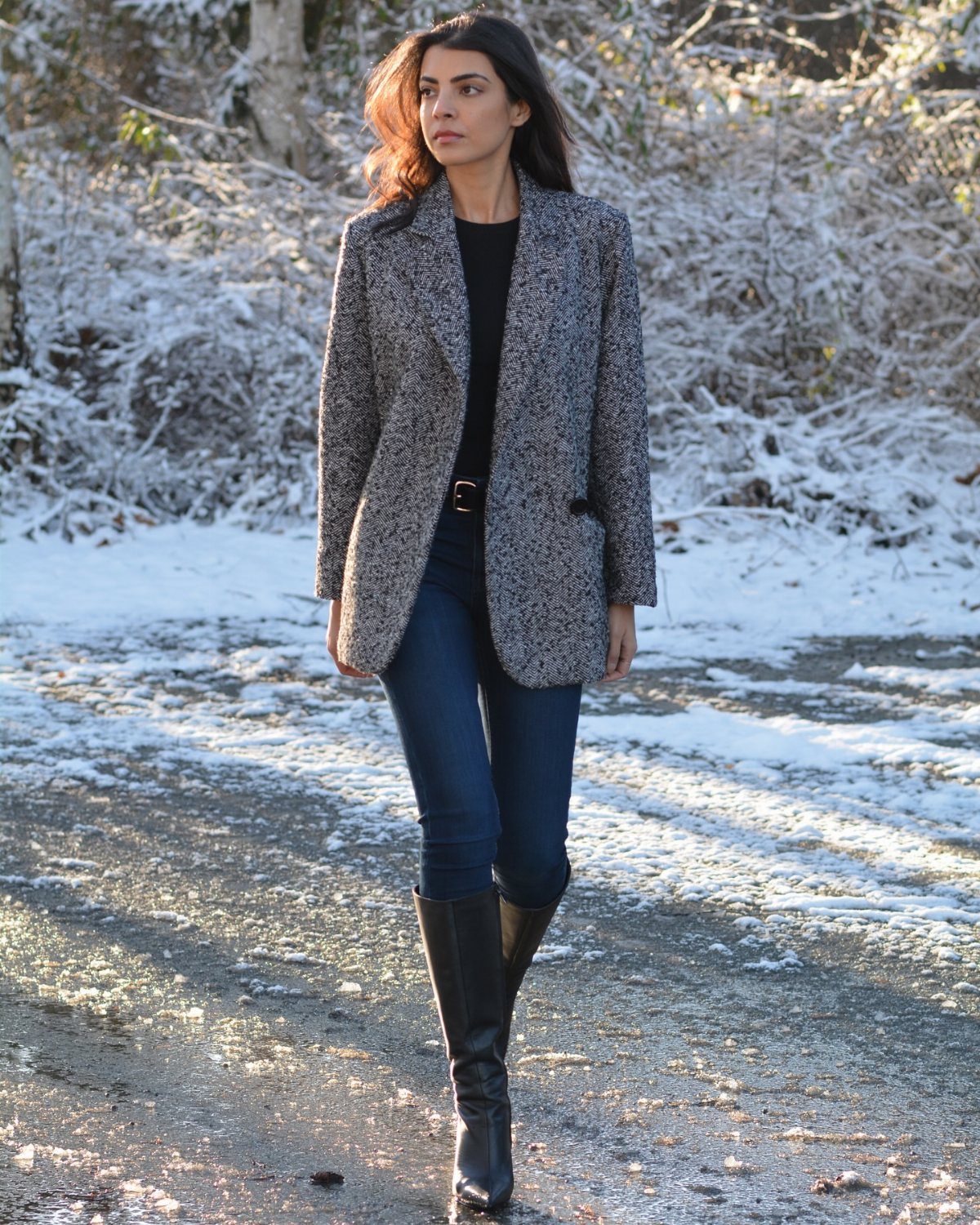 Woman in tweed blazer and skinny jeans tucked into knee-high black leather boots.