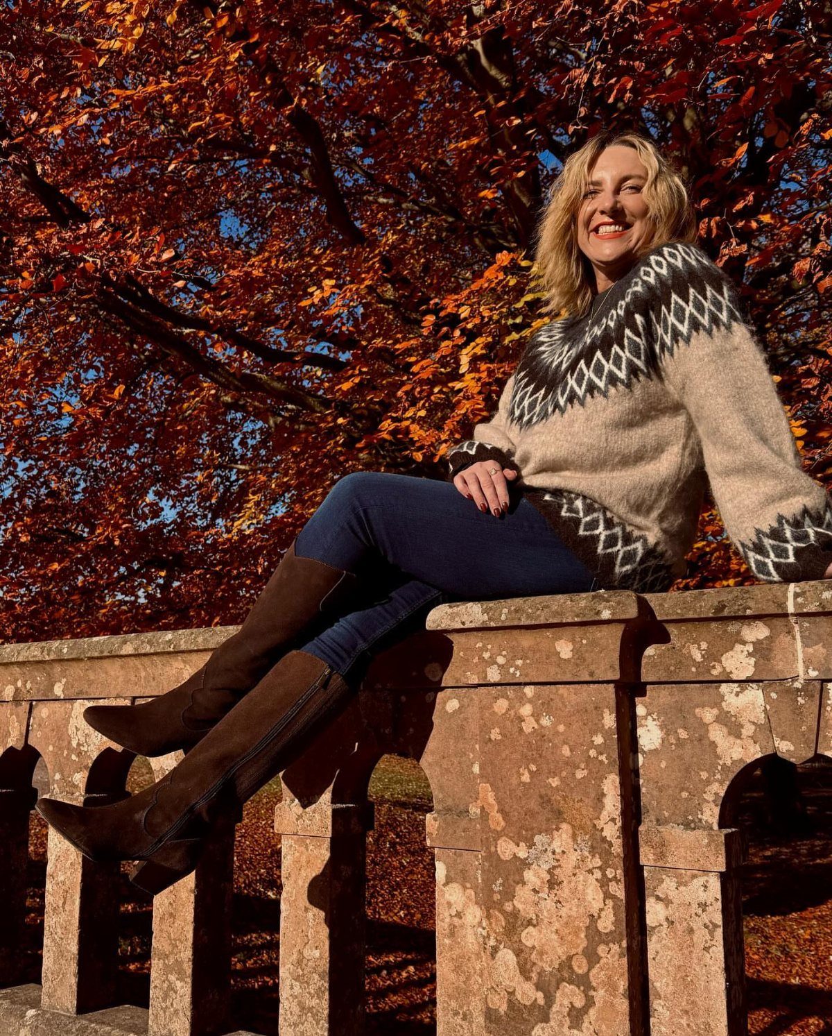 Woman in patterned sweater and slim jeans tucked into brown mid-calf boots.