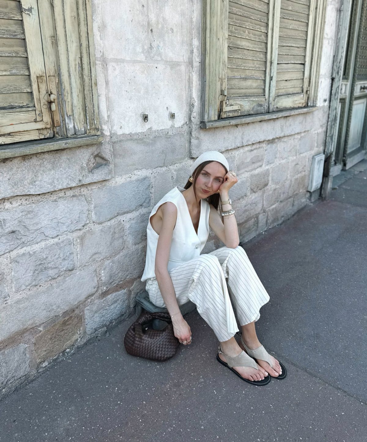Tan Linen Pants Outfit Ideas for Women: 11 Looks to Try 12 Woman wearing white sleeveless top and tan striped linen pants sitting by stone wall